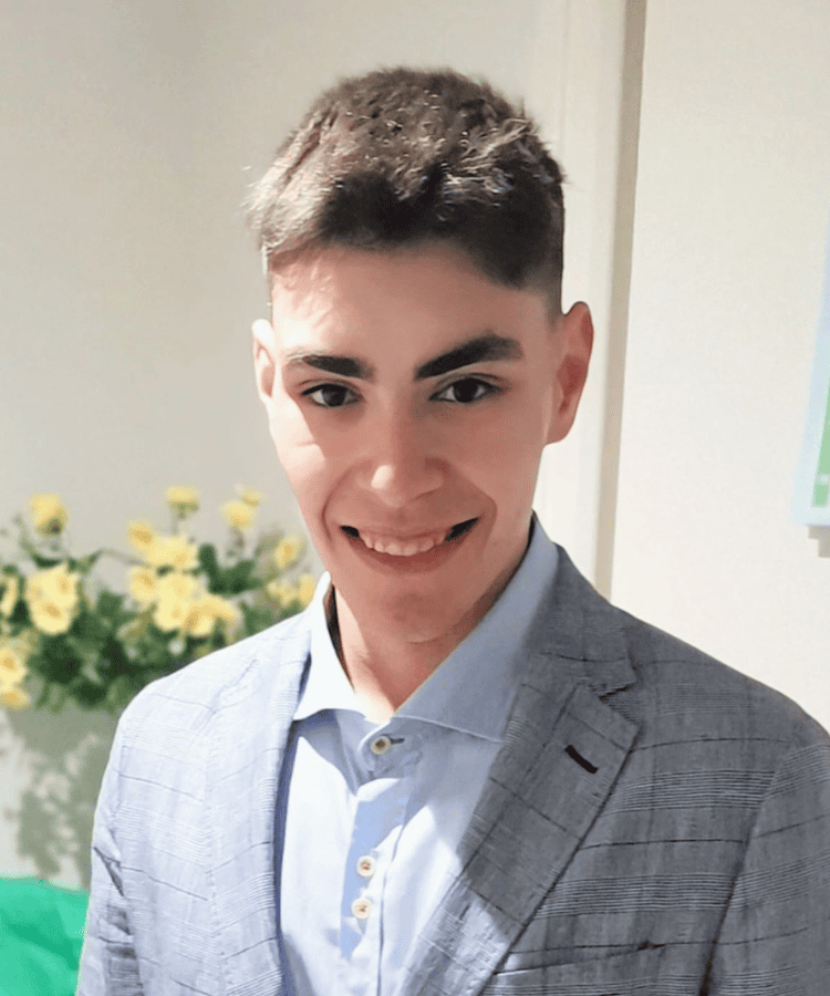 Joven sonriente con chaqueta gris y camisa azul.